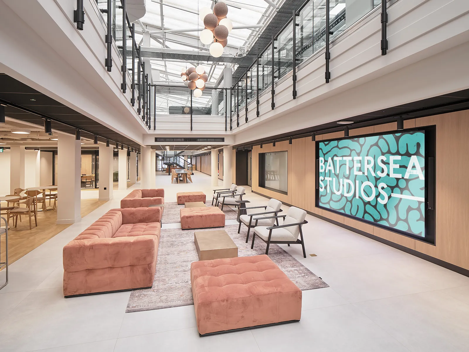 Glass-roofed atrium with sofas and a Battersea Studios screen